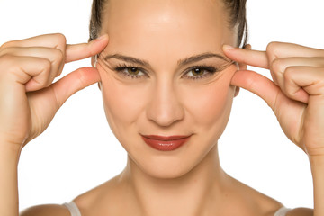 Wall Mural - young woman pinching her eye wrinkles with her fingers on a white background