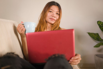 young attractive and beautiful Asian Indonesian woman in jeans and casual top at home working relaxed and happy with laptop computer networking using social media