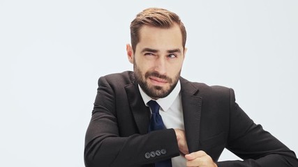 Poster - Cheerful young businessman in black suit and blue tie taking his smartphone out of the inside pocket and having a call over gray background isolated