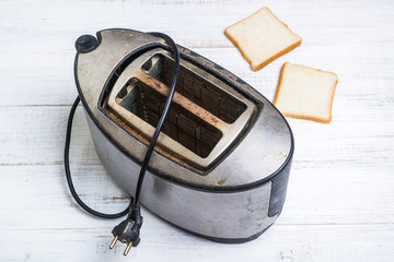 Dirty old toaster with bread on a white wooden background.