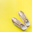 Pair of golden female sneakers on yellow background