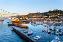 Yachts, Ships And Fishing Boats Berthed At West Mooring Basin Marina Next To The Iconic Astoria Megler Bridge, Commercial Buildings, And Homes On The Coast Hillside.