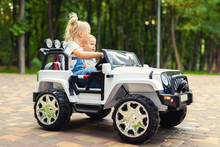 Two Cute Adorable Blond Sibings Children Having Fun Riding Electric Toy Suv Car In City Park. Brother And Sister Enjoy Playing And Driving Vehicle On City Street Outdoor. Happy Childhood Concept