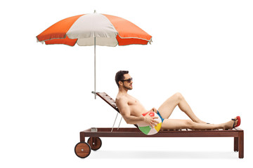 Wall Mural - Young man on a sunbed with an umbrella holding an inflatable ball