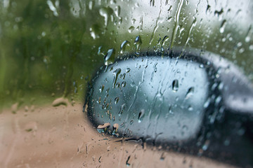 Blurred,rain drops on a car window with the mirror in the background