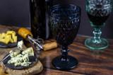 Fototapeta Lawenda - Vintage wine glasses and bottle of red wine on a wooden table. Blue cheese cut on the old cutting board
