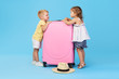 © oes - Happy kids holding colorful pink suitcase prepared for summer vacation. Young travelers. Little girl and boy, sister and brother, having fun isolated on blue background