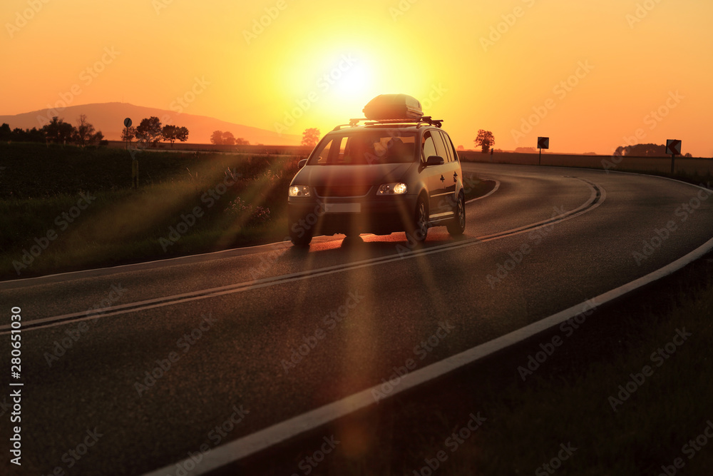 Samochód z bagażnikiem dachowym na zakręcie drogi o zachodzie słońca. - obrazy, fototapety, plakaty 