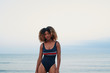 © guille Faingold/Stocksy - Sexy woman with afro in swimsuit against the sea.