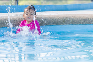 Baby girl of two years old splashes water in a swimming pool. She is happy and playful with her experience.