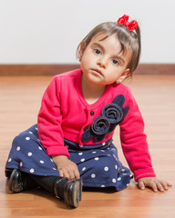 Baby girls of two poses for studio portraits. She is sitting on the floor.