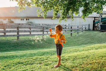 Candid portrait of cute preschool Caucasian child boy blowing soap bubbles in park at summer sunset. Real authentic happy childhood moment. Lifestyle funny children activity.