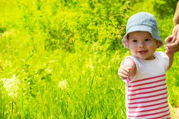 Baby girl 11 months walking on a green meadow close-up. Cheerful laughing child, summer walk, portrait