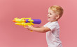 © oes - Happy little toddler boy  in summer clothes holds toy water gun isolated on pink wall background. Children studio portrait. People childhood lifestyle concept.