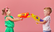 © oes - Happy little toddler boy and girl  in summer clothes holds toy water guns isolated on pink wall background. Children studio portrait. People childhood lifestyle concept.