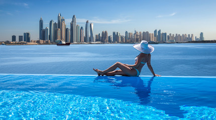 Wall Mural - Beautiful panorama of Dubai Marina skyline in a background with a pool, deck chair and woman with a white hat.