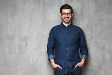 Wall Mural - Young cheerful man wearing trendy denim casual shirt, standing against gray wall with copy space on left side