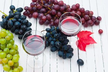 two glasses of red wine and grapes on white wooden table background