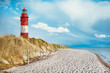 Leuchtturm am Strand einer Insel, an der Küste hinter und auf Düne mit Strandsand und Wasser am Meer. blauer Himmel mit weißen Wolken mit Platz für Text