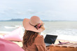 Asian traveler woman with hat and laptop looking sea.