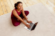 © Anatoliy Karlyuk - Top view of happy energetic young dark skinned woman with beaming smile sitting on carpet with generic portable computer, checking email after indoor training. Sports and active lifestyle concept