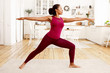 © Anatoliy Karlyuk - Fitness, training, health and wellness concept. Side view of athletic young Afro American housewife in stylish sportswear practicing yoga in the morning, doing warrior 2 pose on mat in kitchen