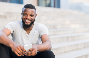 Portrait of casual african guy sitting on stairs and smiling