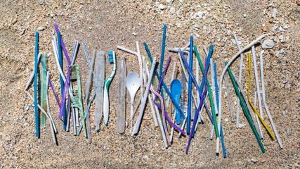 Heap of different plastic waste: straws and single-use spoons, toothbrush and comb collected on the beach on sand background. Environmental pollution problem, a lot of disposable waste, say no plastic