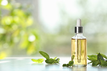 Bottle Of Mint Essential Oil On White Wooden Table Against Blurred Background. Space For Text