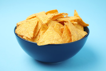 Bowl of tasty Mexican nachos chips on light blue background