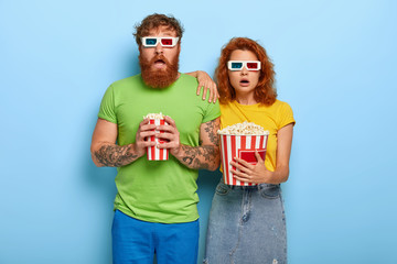 Frightened red haired woman and man being deeply impressed by film, forget they are in cinema, watch horror movie with unexpected ending, enjoy eating popcorn. This evening show grab our attention.