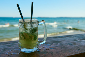 A steamed glass of Mojito on the bar with two black tubes.Against the sea and blue sky.