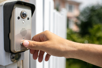 Human finger pushing button of video intercom equipment. Country house background