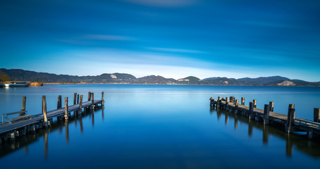 Two Wooden pier or jetty and on a blue lake sunset and sky reflection on water. Versilia Tuscany, Italy