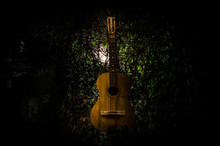 An Wooden Acoustic Guitar Is Against A Grunge Textured Wall. The Room Is Dark With A Spotlight For Your Copyspace.