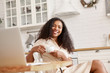 © Anatoliy Karlyuk - Beautiful amazing young stylish African American woman in beige shirt relaxing at home with cup of coffee. Cute dark skinned drinking tea in kitchen, holding white mug, sitting comfortably at table