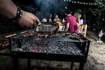 Group of friends making barbecue in the backyard at dinner time