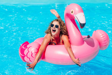 Blonde Girl  Resting  In The  Summer Pool On An Inflatable Pink Flamingo In A Bathing Suit.