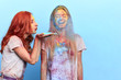 © alfa27 - ginger girl blowing colored powder to her friend's face. close up portrait, isolated blue background, studio shot. copy space. girl makes her best friend laughing