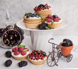 Cupcakes with summer berries raspberries, currants and blackberries on a light background. Assorted summer cakes. Selective focus