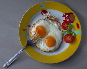 A quick breakfast of two eggs, scrambled eggs with tomatoes on a round plate on a gray background, shot from the top angle