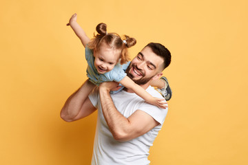 cheerful happy man teaching sweet lovely daughter to fly like a plane. close up photo. isolated yellow background. studio shot, happy moments with best father