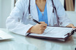 © rogerphoto - Doctor woman filling up medical form while sitting at the table, close-up of hands