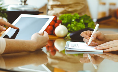 Wall Mural - Close-up of human hands using tablet or touch pad. Two women in kitchen. Cooking, friendship or family fun concepts