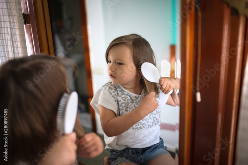 Cuadros en Lienzo funny girl child combing hair in front of mirror