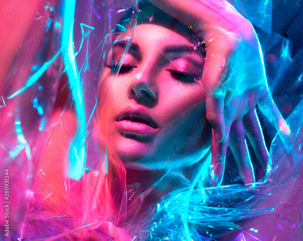Fashion model woman in colorful bright neon lights posing in studio through transparent film. Portrait of beautiful sexy girl in UV. Art design colorful makeup - obrazy, fototapety, plakaty 