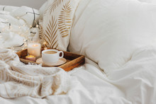 Wooden Tray Of Coffee And Candles On Bed. White Bedding Sheets With Striped Blanket And Pillow. Breakfast In Bed. Hygge Concept.