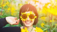 Close Up Creative Portrait Of A Beautiful Young Smiling Happy Brunette Girl With Yellow Flower Petals Under Sunglasses On Background Of A Field Of Sunflowers. Woman Summer Lifestyle And Healthy Teeth.