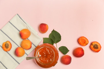 Jar of apricots jam and fresh apricots on pink background, top view with copy space.