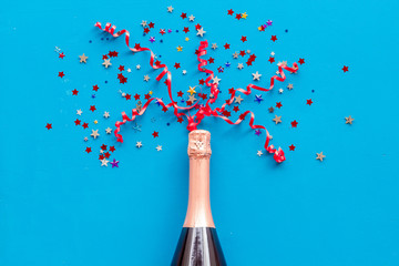 Party with champagne bottle and colorful party streamers on blue background top view